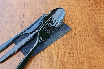 a set of black plastic dishes made of a knife, fork and spoon lies on a paper napkin on a brown wooden table