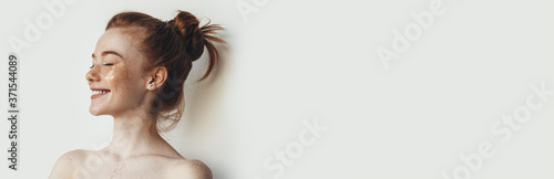 Side view photo of a ginger freckled caucasian woman with hydrogel eye patches and naked shoulders posing on a white studio wall