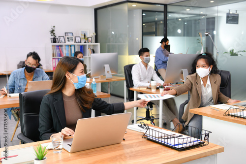 Asian office workers wearing face masks working in new normal office and doing social distancing during corona virus covid-19 pandemic