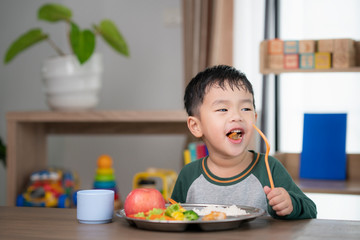 Asian student take a lunch in class room by food tray prepared by his preschoo