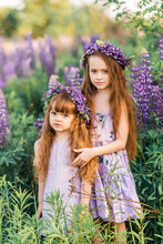 Two Girls With Flowers In Their Hair Among The Flowers. Sunny Summer Photo Of Two Sisters