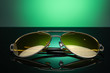 sunglasses with yellow lenses on dark glass with green glare on green background