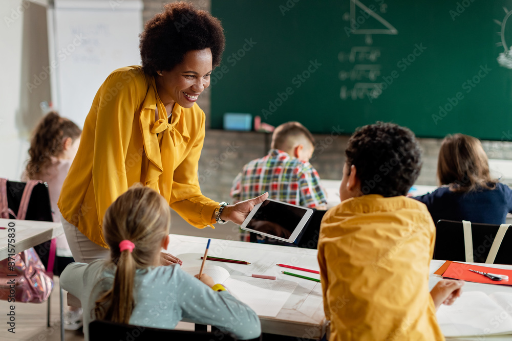 Happy black teacher and elementary students using digital tablet in the ...
