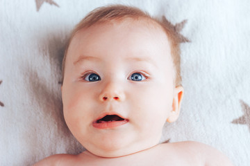 Wall Mural - Photo of a baby with the emotion of surprise, a newborn baby with blue eyes and blond hair lying on a light blanket with brown stars.