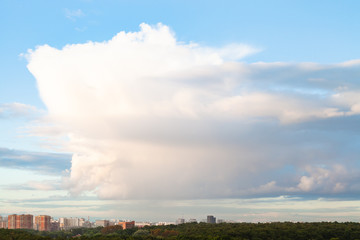 Wall Mural - large cloud in blue sky over city and urban park in summer evening
