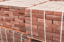 Pallets And Packages Of Freshly Produced Red Bricks In A Construction Warehouse On The Street. Concept Of Repair And Building Materials