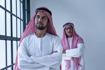 Wall Mural - Portrait of senior and young Arab businessman with arms crossed and standing near window