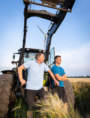 Wall Mural - Agrarpolitik und Getreidemarkt - Landwirt und sein Sohn stehen sorgenerfüllt vor einem Traktor im Getreidefeld.