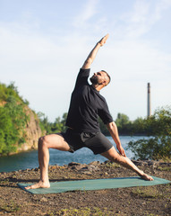 Man doing yoga exercise on the quarry lake at sunny day. International Day of Yoga.