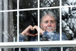 © soupstock - Bearded senior man making heart symbol with hands at the window