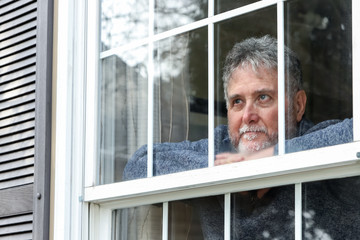 Senior man inside looking out window during quarantine