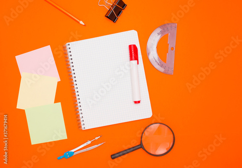 The concept of training and education. Three empty square notes, an empty checkered notebook, and office supplies on an orange background. The view from the top.