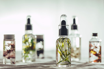 Transparent Bottles of essential oil with fresh herbs.