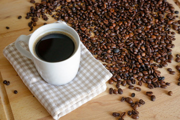 Wall Mural - Coffee grains with white cup on coffee on wooden table, natural light