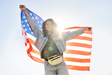 Smiling Young African Woman Holding Usa Flag Dancing Under Sunny Sky Looking At Camera. Happy Free Independent Patriot Afro American Girl Waving United States Flag Dancing Outdoor Feeling Freedom.