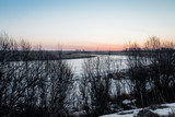 Fototapeta Natura - Landscape. Early spring morning. Gray ice on the river, silhouettes of bushes and trees, blue sky.