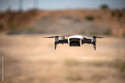 Cuadros en Lienzo Drone blanco con cuatro hélices volando a baja altura en un paisaje desértico, c