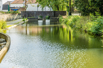 Weir with its stone wall and two floodgates on the Jeker river in the city park of Maastricht, sunny summer day with a beautiful reflection on the water in South Limburg, the Netherlands