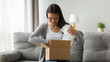 © fizkes - Happy young pretty woman sitting on comfortable sofa, unwrapping cardboard box with ordered online goods at home. Smiling millennial pleasant girl unpacking parcel with sale internet purchase.