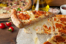 Slice Of Hot Pizza With Melting Cheese And Chorizo On Rustic Wooden Table With Ingredients