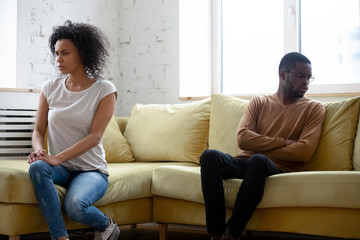 Sticker - Breaking up is never easy. Frustrated upset young african couple of spouses or lovers sitting on sofa apart after having family fight or dispute with mutual insults avoiding look or talk to each other