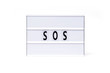 Sos. Text on a vintage lightbox display placed on a white table on a light background. 