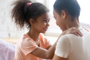 Wall Mural - Trusting relations. Affectionate loving black mommy or elder sister and school age girl hugging and looking in eyes of one another, african mom and preteen daughter enjoying happy moments together