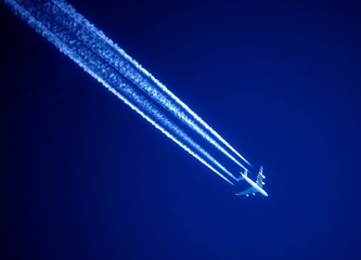 Awesome white jet trails in a dark blue sky and a white airplane 
