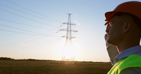 Wall Mural - a close up of a worker adjusts the orange safety helmet on his head and looks at the wires of the hi