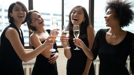 Wall Mural - Happy multiethnic girls wearing elegant little black evening or cocktail dresses toasting clinking holding champagne glasses celebrating birthday enjoy bachelorette party, hangout best friends concept