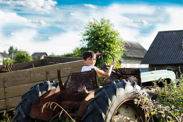 A 10-year-old school-age boy tries to start an old tractor or car. Repair. Little helper. Harvest time. Raising sons by father. Photo. Family farmer