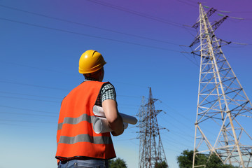 Professional electrician with papers near high voltage tower