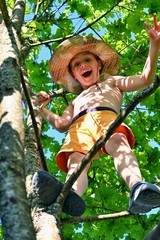 Little boy in hat sitting on tree on sunny summer day