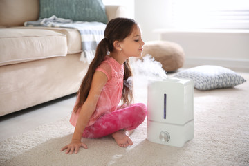 little girl near modern air humidifier at home