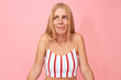 © Anatoliy Karlyuk - Studio shot of emotional timid European teenage girl in stylish striped top shrugging shoulders, doesn't know how to react, being embarrassed or shy. Confused young woman against pink wall background
