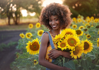 happy young black woman walks in the sunflower field. smiling dark-skinned girl with with a bouquet 