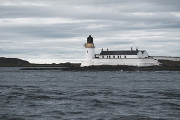 Rocky shores (cliffs) of the west coast of Jura island, a view from the yacht. White lighthouse close-up. Dramatic clouds after the storm. Inner Hebrides, Scotland, UK. Atmospheric landscape