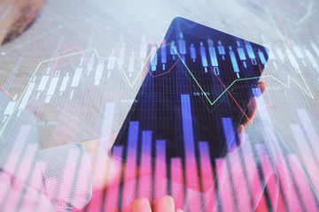 Double exposure of man's hands holding and using a digital device and forex graph drawing. Financial market concept.