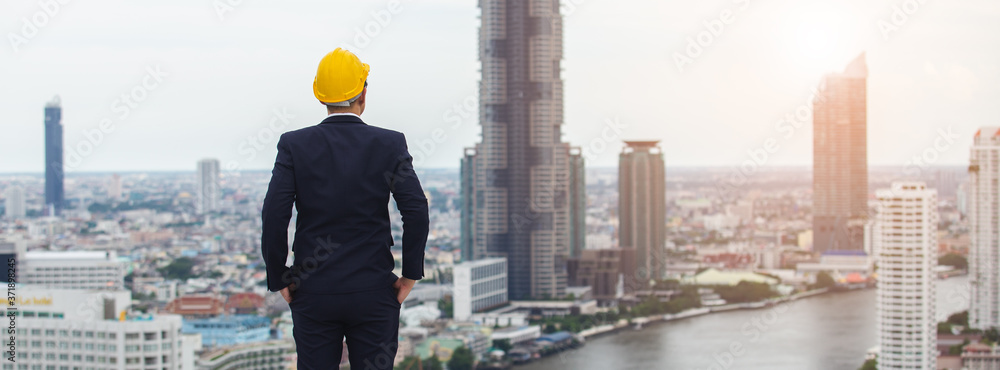 Obraz na płótnie architect man wear black suit and yellow helmet view from back standing on building looking for cityscape. looking for future concept. w salonie