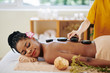 © DragonImages - Beautician putting hot basalt stones along the spine of relaxed pretty young Black woman