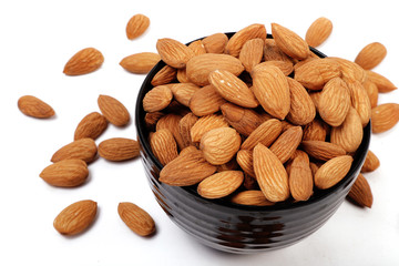 Group of almonds inside and outside bowl isolated on white.