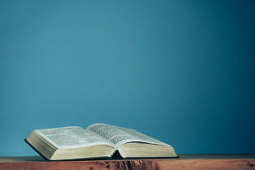 Open Holly Bible on a red wooden table. Beautiful blue wall background. Religious concept.