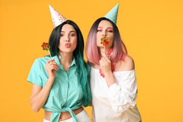 Wall Mural - Beautiful young women in party wigs and with lollipops on color background