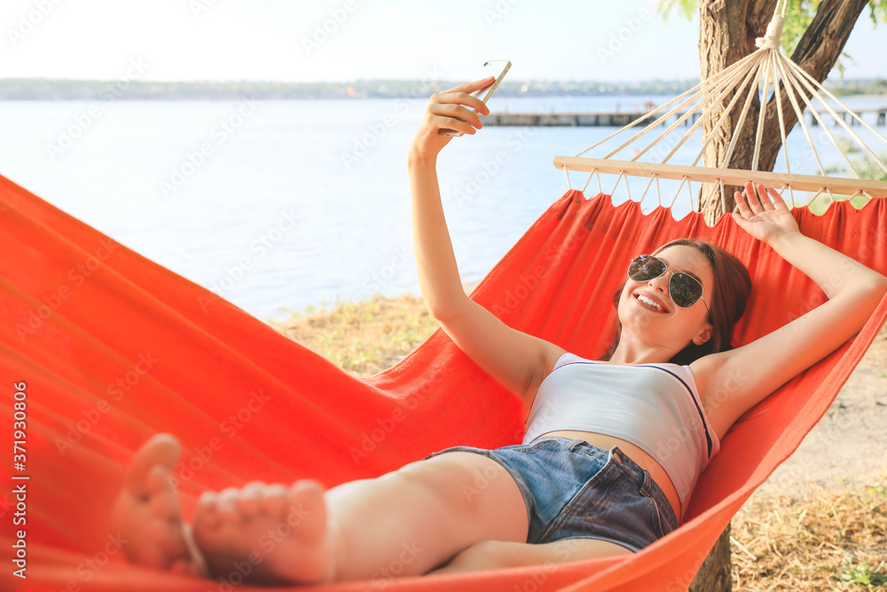 Young woman taking selfie while relaxing in hammock outdoors