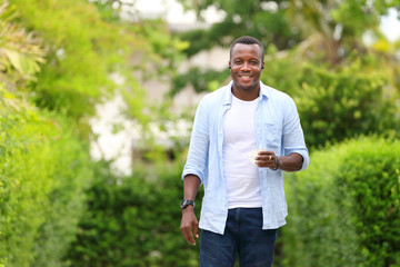 Healthy African American man holding a cup of coffee while walking in relaxation around the neighborhood with good green environment surrounding with copy space