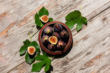 Wall Mural - Ripe purple fig fruit with leaf in a wooden bowl on wooden background. Harvest and healthy eating concept. Selective focus. Top view.