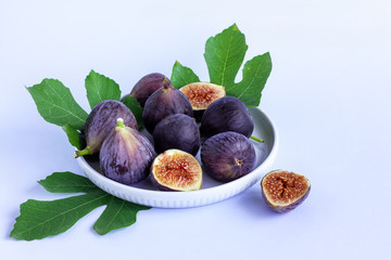 Wall Mural - Ripe purple fig fruit with leaf in a wooden bowl on light blue background. Harvest and healthy eating concept. Selective focus