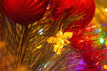 Red Christmas balls and a golden angel hanging on a Christmas tree against a background of decorations and colorful lights