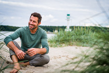 Mann Im Besten Alter Und Sportiv Leger Gekleidet Sitzt An Strand Und Harmoniert Mit Dem Hintergrund