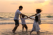 © tirachard - Asian young happy family enjoy vacation on beach in the evening. Dad, mom and kid relax playing together near sea when sunset while travel holiday. Lifestyle travel holiday vacation summer concept.